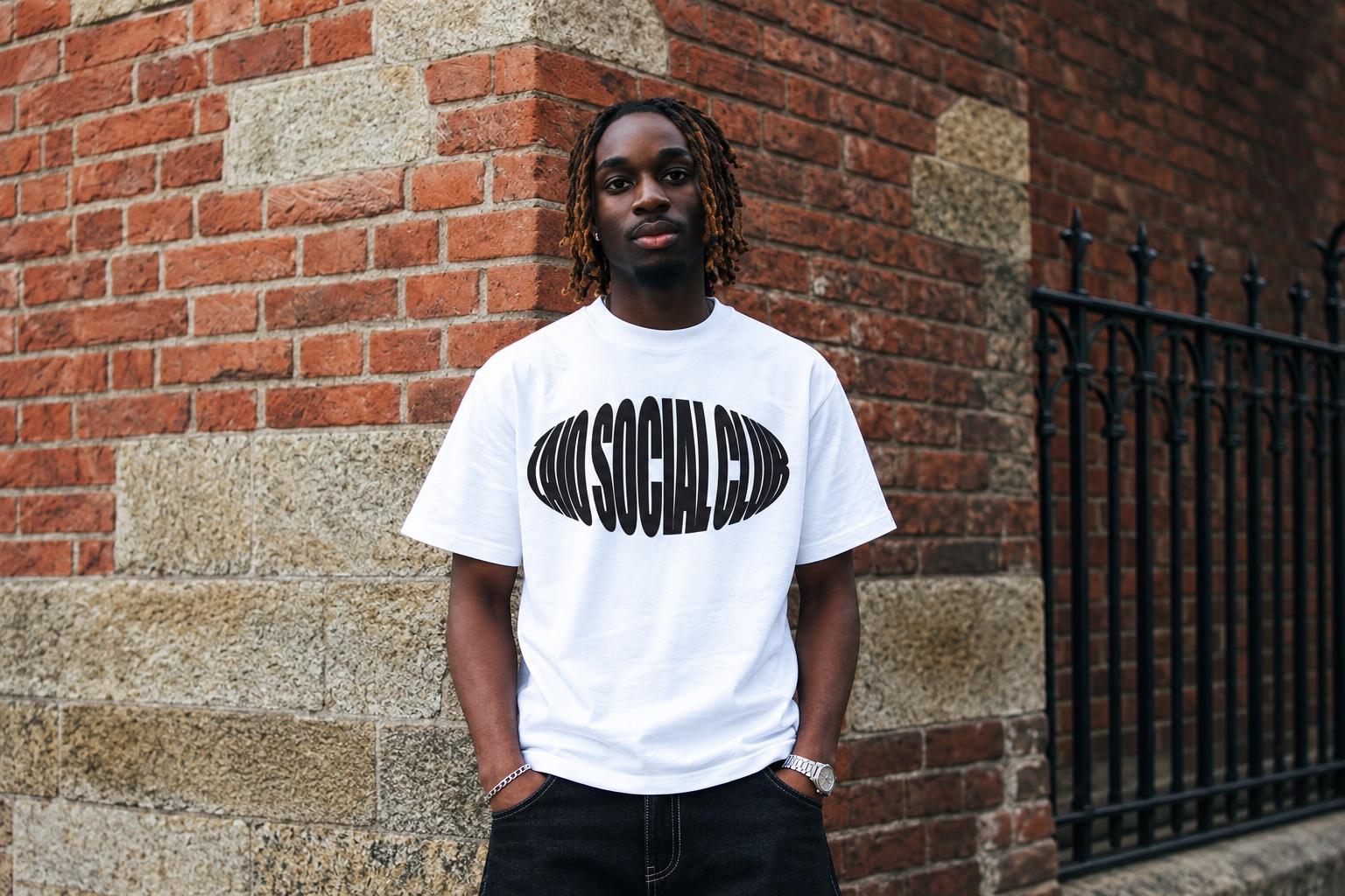 Model wearing the white Zaio Social Club tee, standing against a brick wall